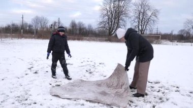 Bir kadın ve oğlu karda halı temizler ve eğlenirler..