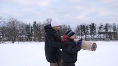 Bir kadın ve oğlu karda halı temizler ve eğlenirler..