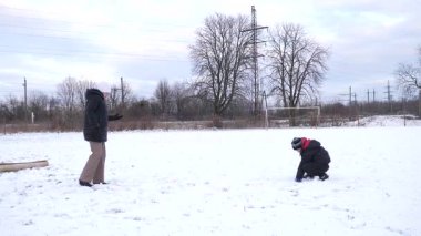 Bir kadın ve oğlu karda halı temizler ve eğlenirler..