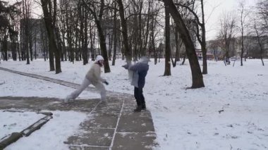 Küçük kardeşiyle bir kız karlı bir parkta yürüyor ve eğleniyor..