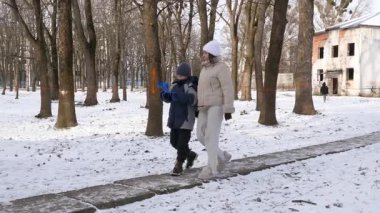 Küçük kardeşiyle bir kız karlı bir parkta yürüyor ve eğleniyor..