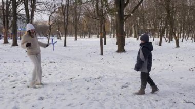 Küçük kardeşiyle bir kız karlı bir parkta yürüyor ve eğleniyor..