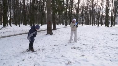 Küçük kardeşiyle bir kız karlı bir parkta yürüyor ve eğleniyor..