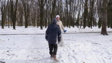 Küçük kardeşiyle bir kız karlı bir parkta yürüyor ve eğleniyor..