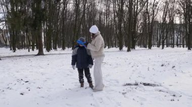 Küçük kardeşiyle bir kız karlı bir parkta yürüyor ve eğleniyor..