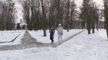 Küçük kardeşiyle bir kız karlı bir parkta yürüyor ve eğleniyor..