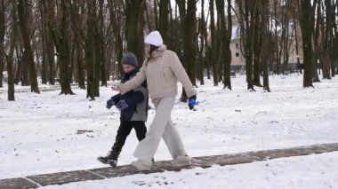 Küçük kardeşiyle bir kız karlı bir parkta yürüyor ve eğleniyor..