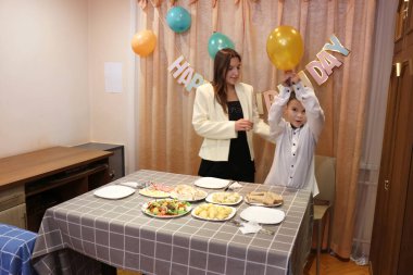 Bir anne, kızı ve oğluyla birlikte doğum günü kutlaması için şenlik masasına servis yapıyor. Yumuşak ışıklandırma.