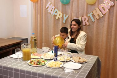 Bir anne, kızı ve oğluyla birlikte doğum günü kutlaması için şenlik masasına servis yapıyor. Yumuşak ışıklandırma.