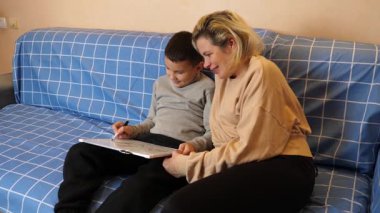 Anne ve oğul kanepede otururken tahta üzerine bir kalemle çizer..