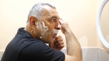 Bir adam tıraş köpüğü ve traş köpüğünü banyoda jiletle kullanıyor..