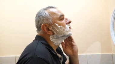 Bir adam tıraş köpüğü ve traş köpüğünü banyoda jiletle kullanıyor..