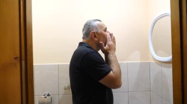 Bir adam banyoda tıraş losyonu kremi kullanıyor..