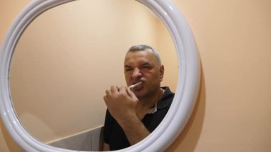 Bir adam dişlerini banyoda fırçalıyor..