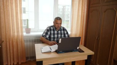 Bir adam dizüstü bilgisayarla masada otururken çalışıyor..