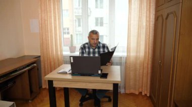 Bir adam dizüstü bilgisayarla masada otururken çalışıyor..