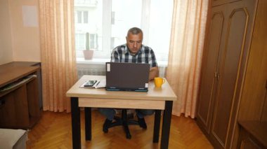 Bir adam dizüstü bilgisayarla masada otururken çalışıyor..