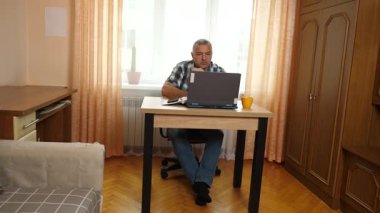 Bir adam dizüstü bilgisayarla masada otururken çalışıyor..