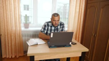 Bir adam dizüstü bilgisayarla masada otururken çalışıyor..