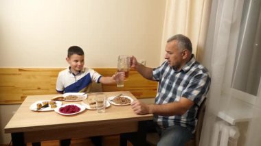 Bir adam ve oğlu mutfak masasında yemek yiyorlar..