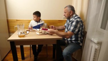 Bir adam ve oğlu mutfak masasında yemek yiyorlar..