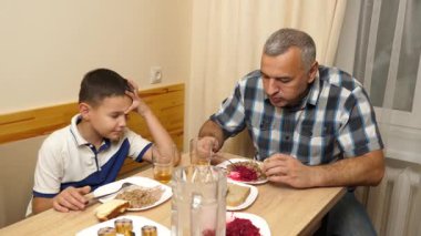 Bir adam ve oğlu mutfak masasında yemek yiyorlar..