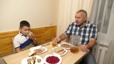 Bir adam ve oğlu mutfak masasında yemek yiyorlar..