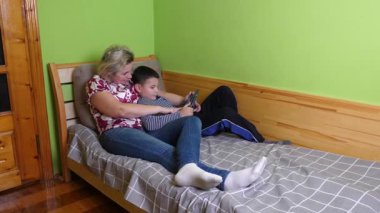 Bir kadın ve oğlu kanepede yatarken aletlerle oyun oynuyorlar..