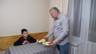 Baba ve oğul mutfak masasında yemek yiyorlar..