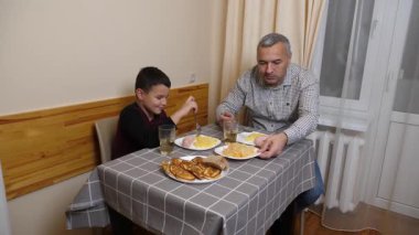 Baba ve oğul mutfak masasında yemek yiyorlar..