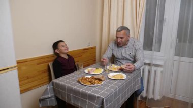 Baba ve oğul mutfak masasında yemek yiyorlar..