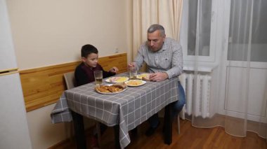 Baba ve oğul mutfak masasında yemek yiyorlar..