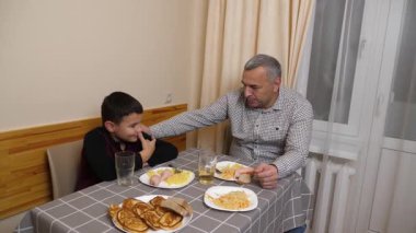 Baba ve oğul mutfak masasında yemek yiyorlar..