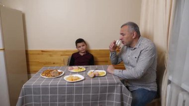 Baba ve oğul mutfak masasında yemek yiyorlar..