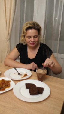 Bir kadın yemek yiyor, mutfak masasında oturuyor..