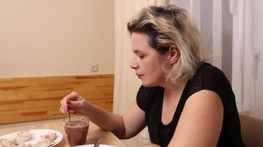 Mutfaktaki masada sandviç yiyip kahve içen bir kadın..