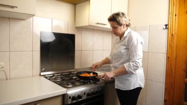 Bir kadın yemek pişirmek için tavada sebze kızartıyor..
