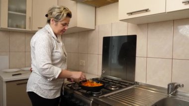 Bir kadın yemek pişirmek için tavada sebze kızartıyor..