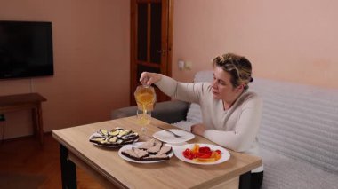 Bir kadın mutfaktaki masada otururken yemek ve içki yer..