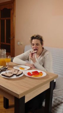 Bir kadın mutfaktaki masada otururken yemek ve içki yer..