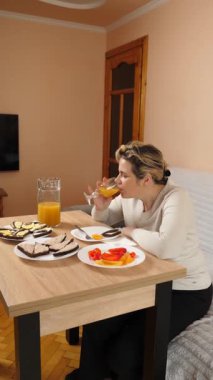 Bir kadın mutfaktaki masada otururken yemek ve içki yer..