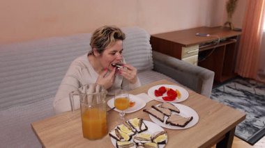 Bir kadın mutfaktaki masada otururken yemek ve içki yer..