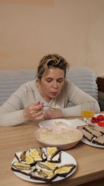 Bir kadın mutfaktaki masada otururken yemek ve içki yer..