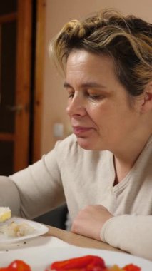 Bir kadın mutfaktaki masada otururken yemek ve içki yer..