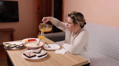 Bir kadın mutfaktaki masada otururken yemek ve içki yer..