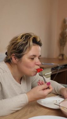 Bir kadın mutfaktaki masada otururken yemek ve içki yer..