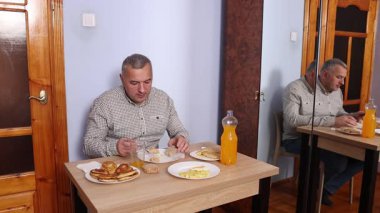 Bir adam masada otururken yemek ve içki yer..