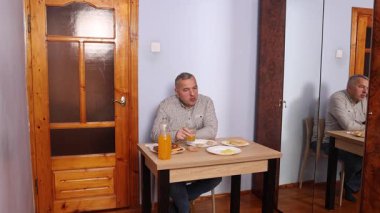 Bir adam masada otururken yemek ve içki yer..