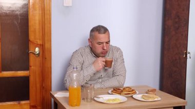 Bir adam masada otururken yemek ve içki yer..