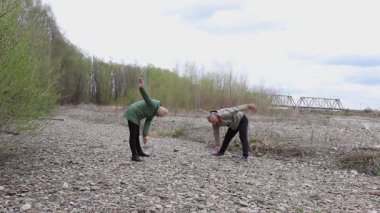 Bir erkek ve bir kadın nehir kenarında fiziksel egzersiz yapıyorlar..